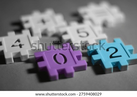 Close-up of interlocking plastic puzzle blocks with numbers and brackets on a gray background, representing coding, education, and creative problem solving.