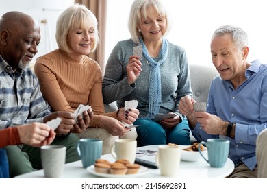 Closeup of international group of cheerful elderly people men and women in casual outfits chilling together at sanatorium, sitting on sofa in living room, playing card games, drinking tea, chatting - Powered by Shutterstock