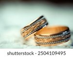 Close-up of intricately designed gold wedding bands on a soft surface. Two elegantly crafted wedding bands feature woven gold and silver designs.