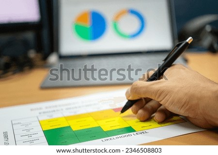 Close-up at the investor hand is using luxury ballpoint pen to write on project investment risk assessment matrix with profit analysis graph in laptop as blurred background. Business work concept.