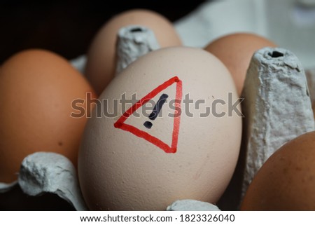 Closeup of isolated raw brown eggs in carton box with warning sign - salmonella infection risk and cholesterol consumption 