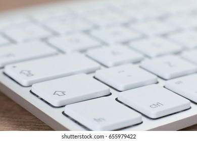 Close-up isometric view of partially blurry white keyboard with many white keys on top of wooden table