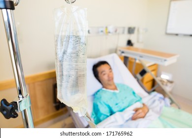 Closeup Of IV Bag With Patient Lying In Background On Hospital Bed