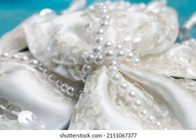 A closeup of an ivory white satin beaded bow for wedding dress trim. Decorated with faux pearls and sequins on turquoise fabric.