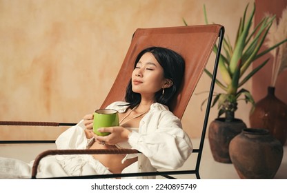 Closeup of japanese model enjoying herbal tea on her lounger, spending weekend at spa resort, taking care of her body and mental health after hard work week - Powered by Shutterstock