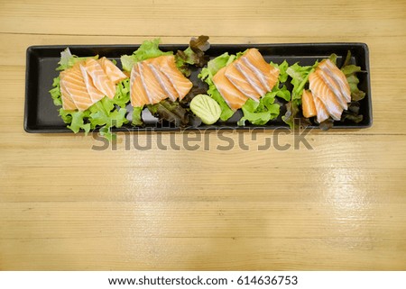 Close-up Japanese sashimi salmon in black bowl decoration with vegetables and wasabi on wooden background.