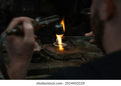 close-up of jeweler's hands working with a blowtorch on a piece of silver jewelry in his workshop. - Powered by Shutterstock