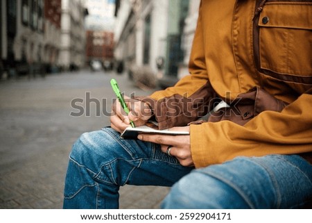Close-up of a journalist meticulously taking notes in a notebook with a green pen, sitting outdoors in a blurred urban environment, capturing details for a news story or article
