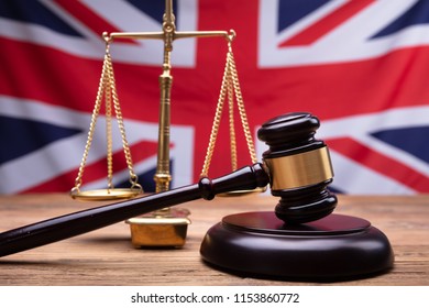 Close-up Of Judge Wooden Gavel And Justice Scale In Front Of UK Flag