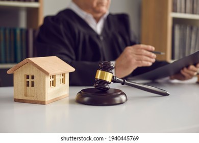 Close-up of judge's gavel, sound block, and small wooden toy house on courtroom table in court. Concept of real estate law, partition of property, separation of estates and divorce settlement
