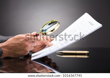 Close-up Of A Judge's Hand Looking At Document With Magnifying Glass