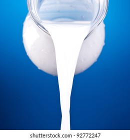 Closeup Of A Jug With Pouring Milk On Blue Background