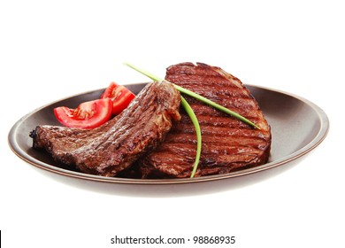 close-up of juicy sirloin beef with pasta tomatoes and green onion on dark dish isolated over white background