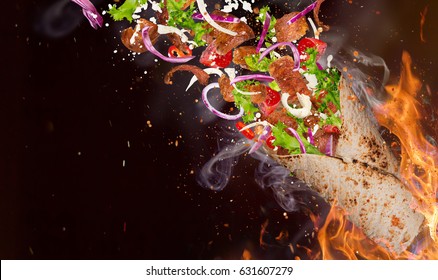 Close-up of kebab sandwich with flying ingredients with fire flames background.