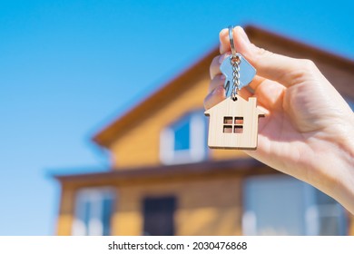 Close-up of a key with a house-shaped keychain in hand. In the background is a house. The concept of buying and insuring real estate, cottage, mortgage. Copy space. - Powered by Shutterstock