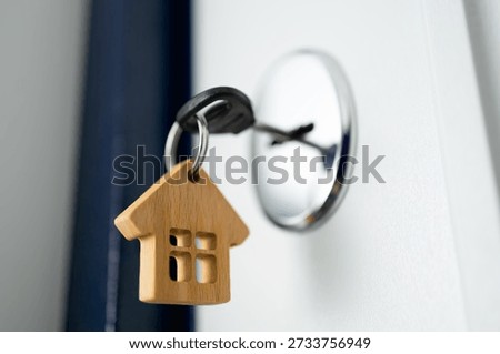 Close-up of a key inserted into a door lock with a wooden house keychain, symbolizing new home ownership, real estate purchase, and property investment.