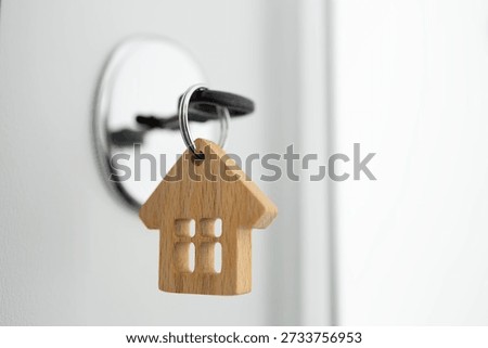 Close-up of a key inserted into a door lock with a wooden house keychain, symbolizing new home ownership, real estate purchase, and property investment.