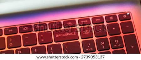 Close-up of a keyboard with the 'BACKSPACE' key highlighted, showcasing modern design elements and vibrant lighting. Ideal for illustrating technology or workspace themes.