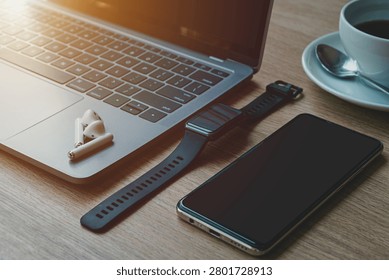 Close-up of Keyboard laptop computer, wireless earphones, smartwatch and smartphone empty screen on wooden background office desk in coffee shop like the background