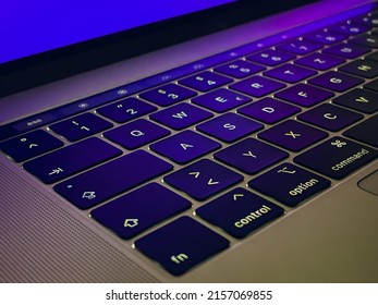 A closeup of a Keyboard of a Notebook with Violet lighting mirrored from the aluminum frame - Shutterstock ID 2157069855
