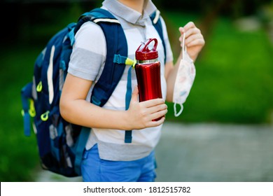 Closeup Of Kid Boy, Medical Mask, Water Bottle And Backpack Or Satchel. Schoolkid On Way To School. Child Outdoors. Back To School After Quarantine Time From Corona Pandemic Disease Lockdown. No Face.