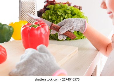 A Closeup Of A Kid Cutting Vegetables A Red Pepper With A Knife Wearing Safety Gloves