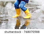 Close-up of kid wearing yellow rain boots and walking during sleet, rain and snow on cold day. Child in colorful fashion casual clothes jumping in a puddle. Having fun outdoors.