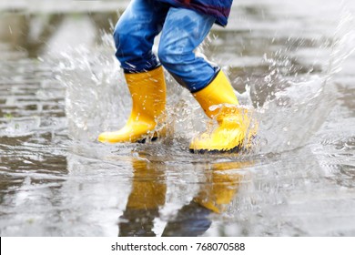 Крупным планом ребенка в желтых дождевых сапогах и ходьбе во время мокрого снега, дождя и снега в холодный день. Ребенок в красочной моде повседневная одежда прыгает в луже. Веселье на открытом воздухе.