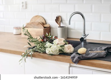 Closeup Of Kitchen Interior. White Brick Wall, Metro Tiles, Wooden Countertops With Kitchen Utensils. Roses Flowers In Black Sink. Modern Scandinavian Design. Home Staging, Cleaning Concept.