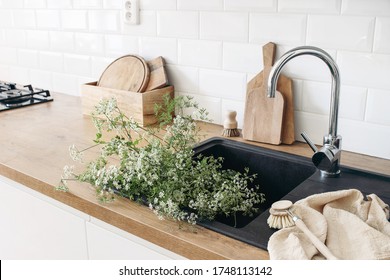 Closeup Of Kitchen Interior. White Brick Wall, Metro Tiles, Wooden Countertops With Chopping Boards. Cow Parsley Plants In Black Sink. Modern Scandinavian Design. Home Staging, Cleaning Concept.