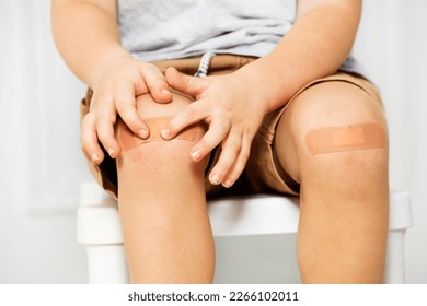 Close-up of a knee of a little boy with patch on it, focus on hands and fingers touching scratch