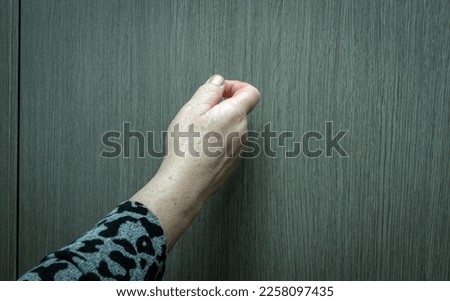 Close-up Knocking on the door of an elderly woman, a woman's hand knocks on a wooden door, a visit to visit. Grandma knocks on the door