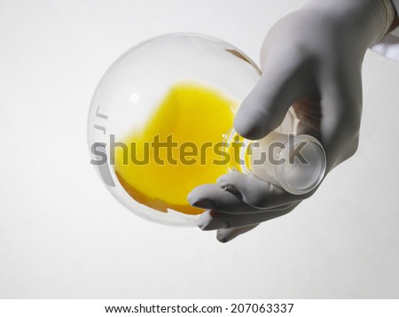 Closeup of lab worker's hand wearing rubber gloves holding flack of yellow solution on white background