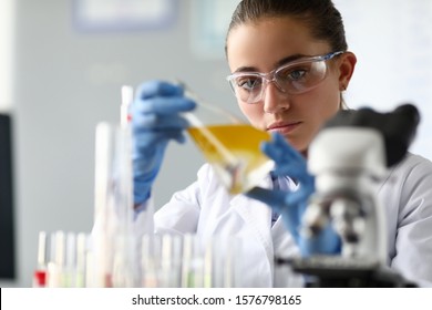 Close-up Of Laboratory Researcher Holding Medical Glass Bottle With Yellow Liquid Wearing Sterile Gloves And Special Lab Eyewear. Scientist Woman At Job. Chemistry Concept