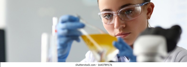 Close-up of laboratory researcher holding medical glass bottle with yellow liquid wearing sterile gloves and special lab eyewear. Scientist woman at job. Chemistry concept
