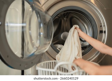 Close-up of Lady loading clothes into front-load washer. Clean, modern environment with solo responsibility.