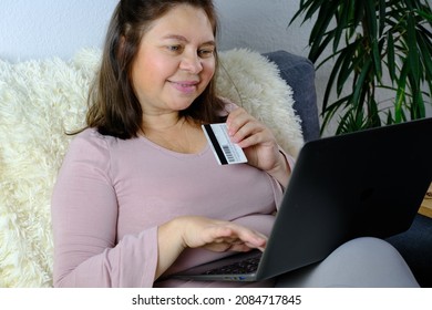 Close-up Of Laptop And Credit Card In Female Hands, Middle-aged Woman Of 50 Years Old In Sits On Sofa, Communicates On Internet, Concept Of Technology, Stay At Home, Business, Online Shopping