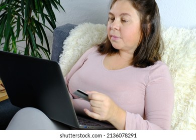 Close-up Of Laptop And Credit Card In Female Hands, Middle-aged Woman Of 50 Years Old In Sits On Sofa, Communicates On Internet, Concept Of Technology, Stay At Home, Business, Online Shopping