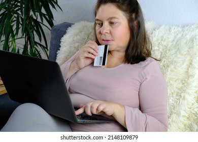 Close-up Of Laptop And Credit Card In Female Hands, Middle-aged Woman Of 50 Years Old In Sits On Sofa, Communicates On Internet, Concept Of Technology, Stay At Home, Business, Online Shopping