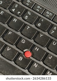 Close-up of a laptop keyboard featuring a red TrackPoint nub, used for cursor control, surrounded by dusty keys—showcasing classic tech design in a modern workspace.