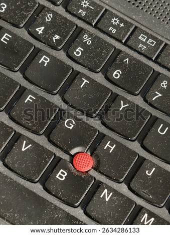 Close-up of a laptop keyboard featuring a red TrackPoint nub, used for cursor control, surrounded by dusty keys—showcasing classic tech design in a modern workspace.