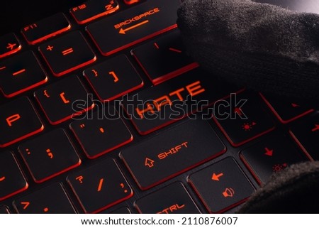 Close-up laptop keyboard with Red  light button Hate. Finger in glove