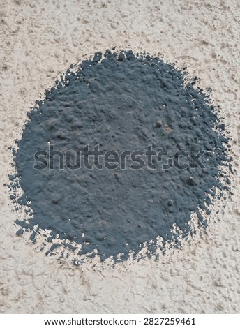 Close-up of a large black painted circle on a rough stucco wall texture with beige plaster background