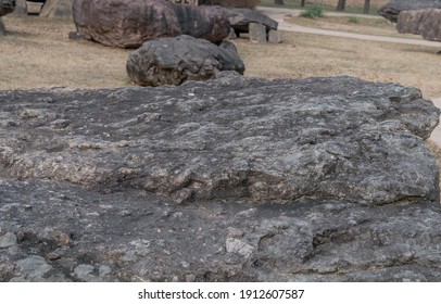 Closeup of large boulder used as capstone on dolmen tomb with similar tombs slightly blurred in background.