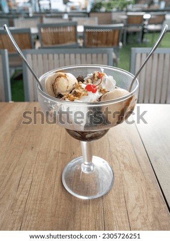 close-up of large dessert cup filled with delicious ingredients such as vanilla ice cream, cream, nuts, brownie pieces and a cherry with two spoons. 