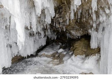Close-up of large icicles and ice formations hanging from a rocky cave with snow and frozen water on the shore of Lake Baikal, Irkutsk Oblast, Russia