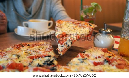 Close-up of large pizza on table. Women's hands tearing off piece of juicy pizza.