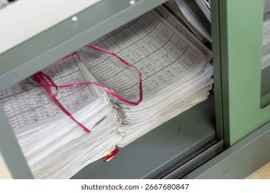 Close-up of a large stack of old printed papers bound with red string inside a green industrial machine or filing system. Represents data processing archives or historical records. - Powered by Shutterstock - Get 15% off with code: PIKWIZARD15