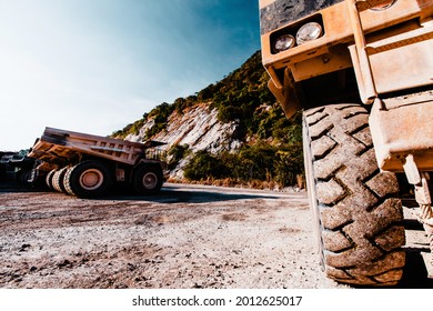 Close-up a large wheel of mining dump truck at an open pit near mountains area, lots of large mining dump truck parked in the backgrounds. Industrial, transportation concepts. Focus on wheel.