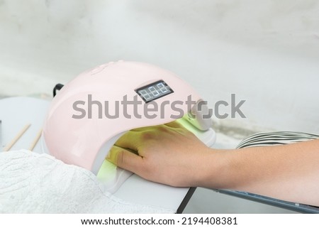 close-up of a latina girl's hand inside a 48 watt led nail lamp for semi permanent acrylic gel. woman getting a manicure for her personal nail care. pink lamp working properly.
